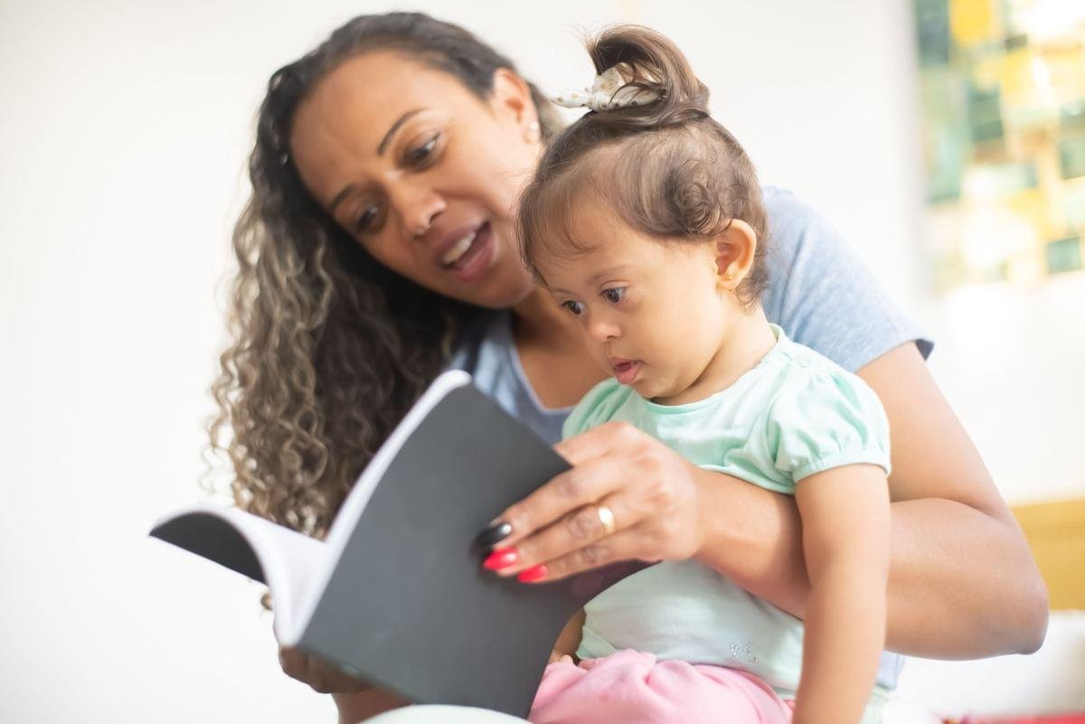 Mãe fazendo devocional infantil com a filha, lendo um livro juntas